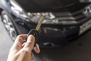 Man hold car remote key for unlock or lock the black car in background.